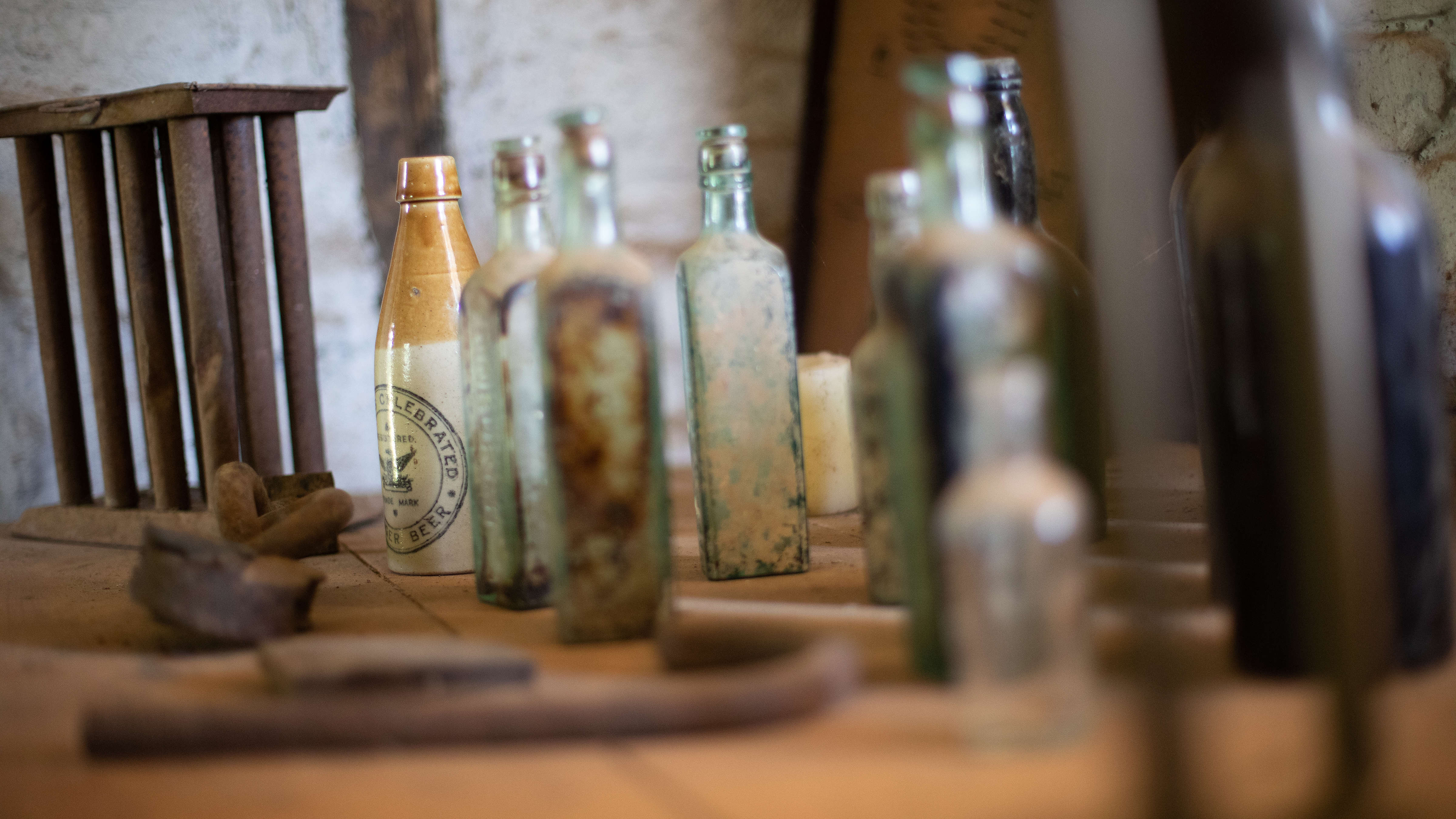 A collection of old glass and pottery bottles on a wooden table with a metal candlestick mould. Photo: Kieran Bradley.