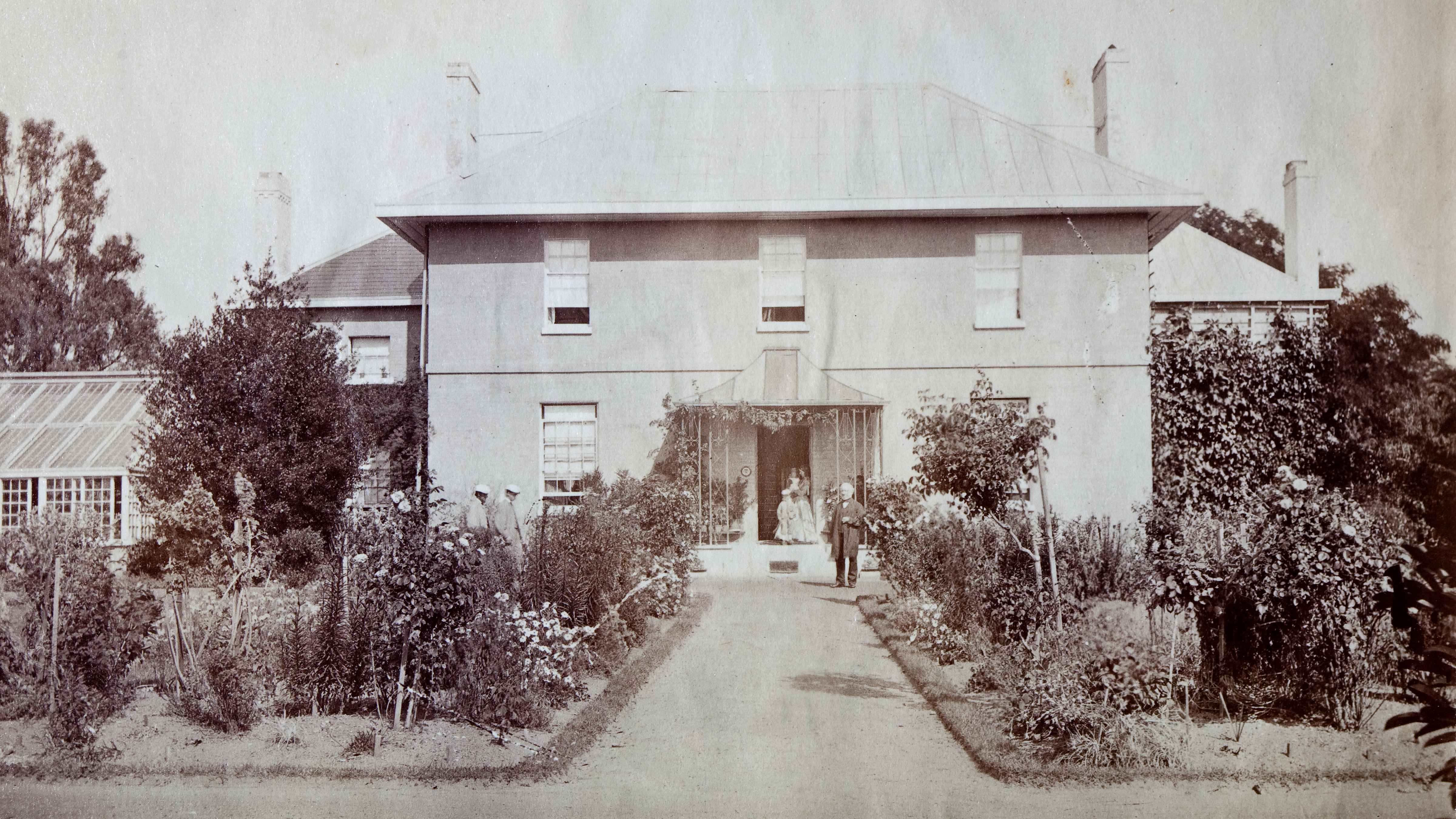 Brickendon Georgian homestead with the first William Archer standing in front of house and family members in the background. Rose gardens with a path in the centre, lead to the house with a greenhouse to the left. Source:Brickendon Estate Archive.
