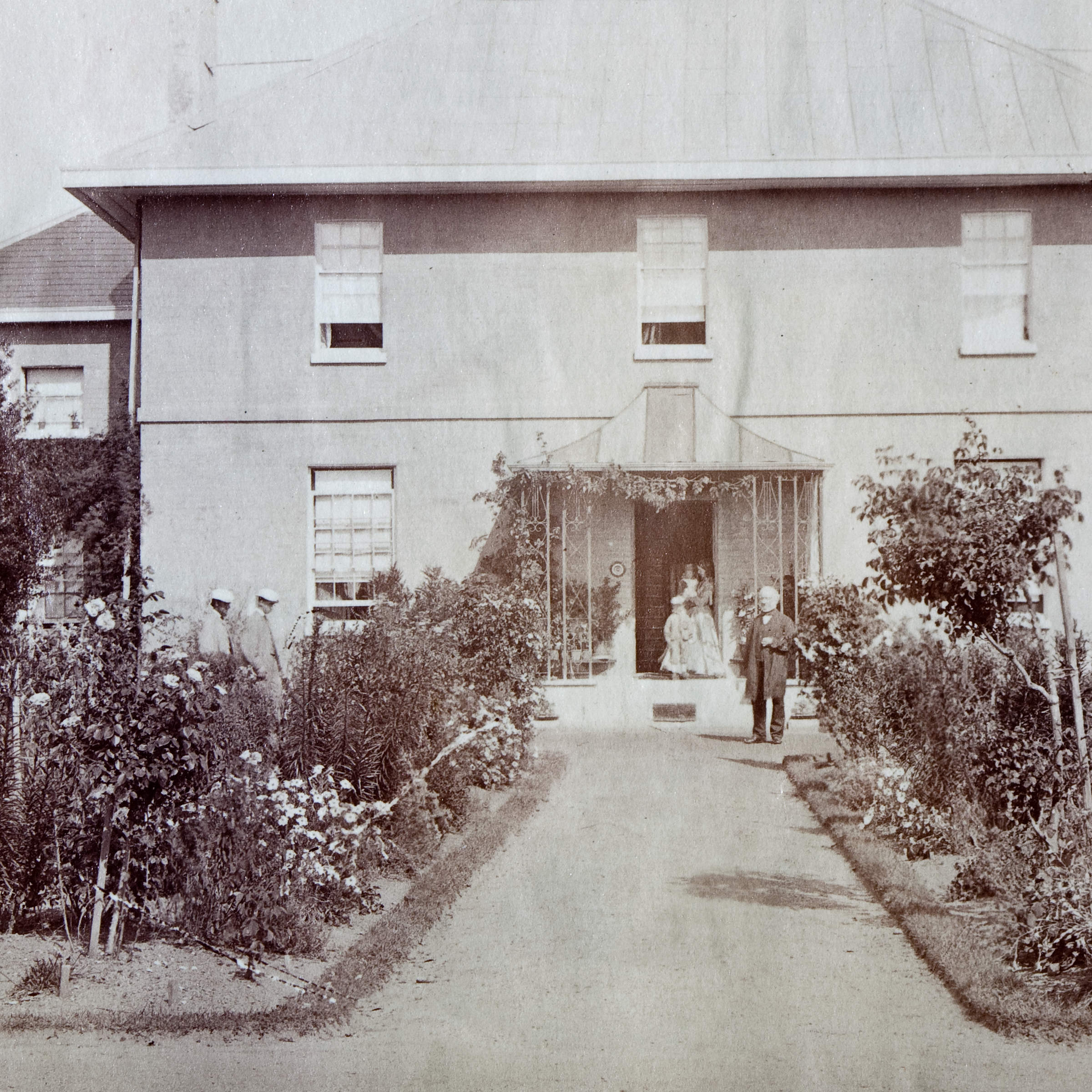 Brickendon Georgian homestead with the first William Archer standing in front of house and family members in the background. Rose gardens with a path in the centre, lead to the house with a greenhouse to the left. Source:Brickendon Estate Archive.