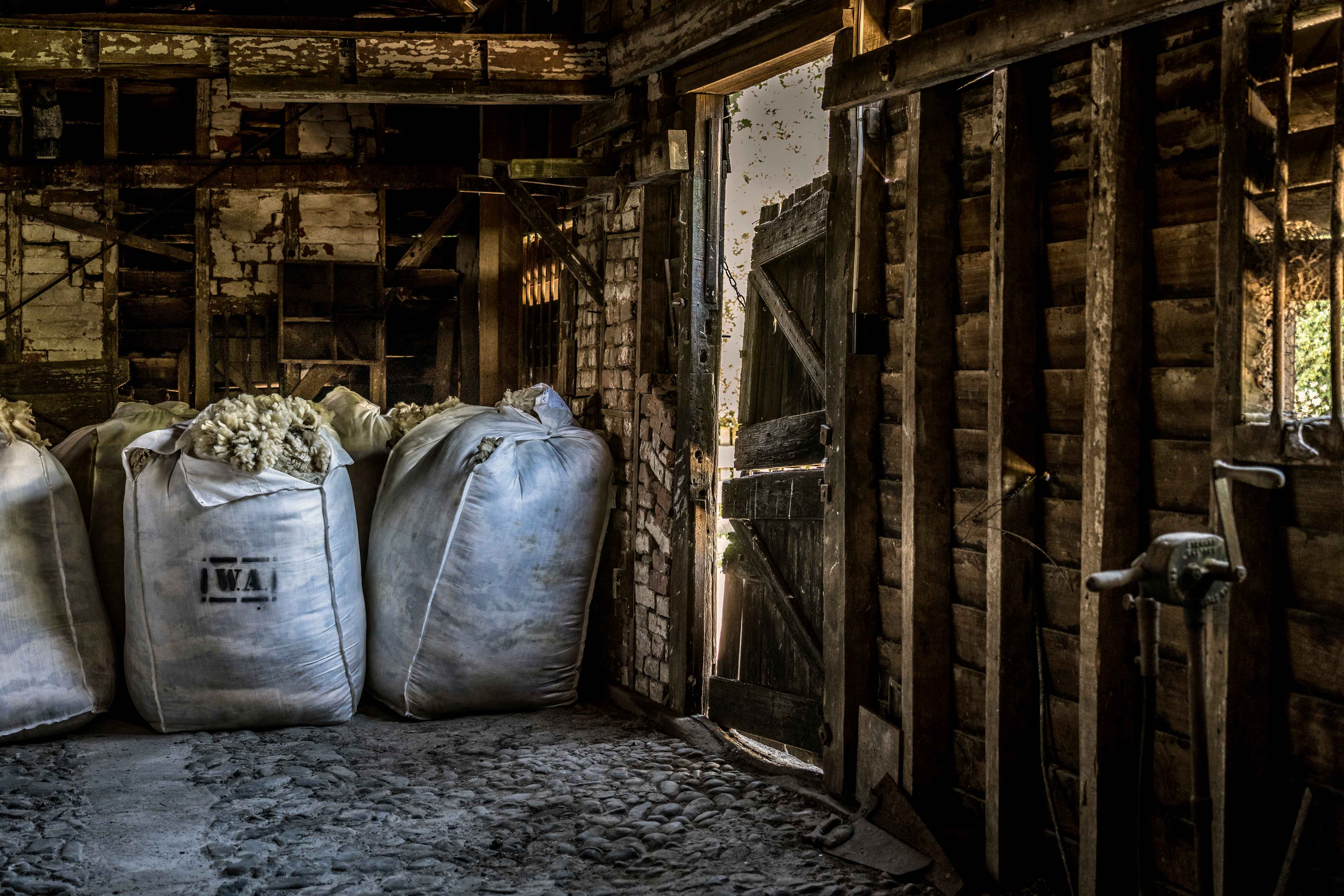 Several open bales of wool, one branded with WA (in a box) brand. The building is the original draught horse stables with stone cobbled floor, timber walls and brick nogging. The split stable door is closed. Photo: Rob Burnett.
