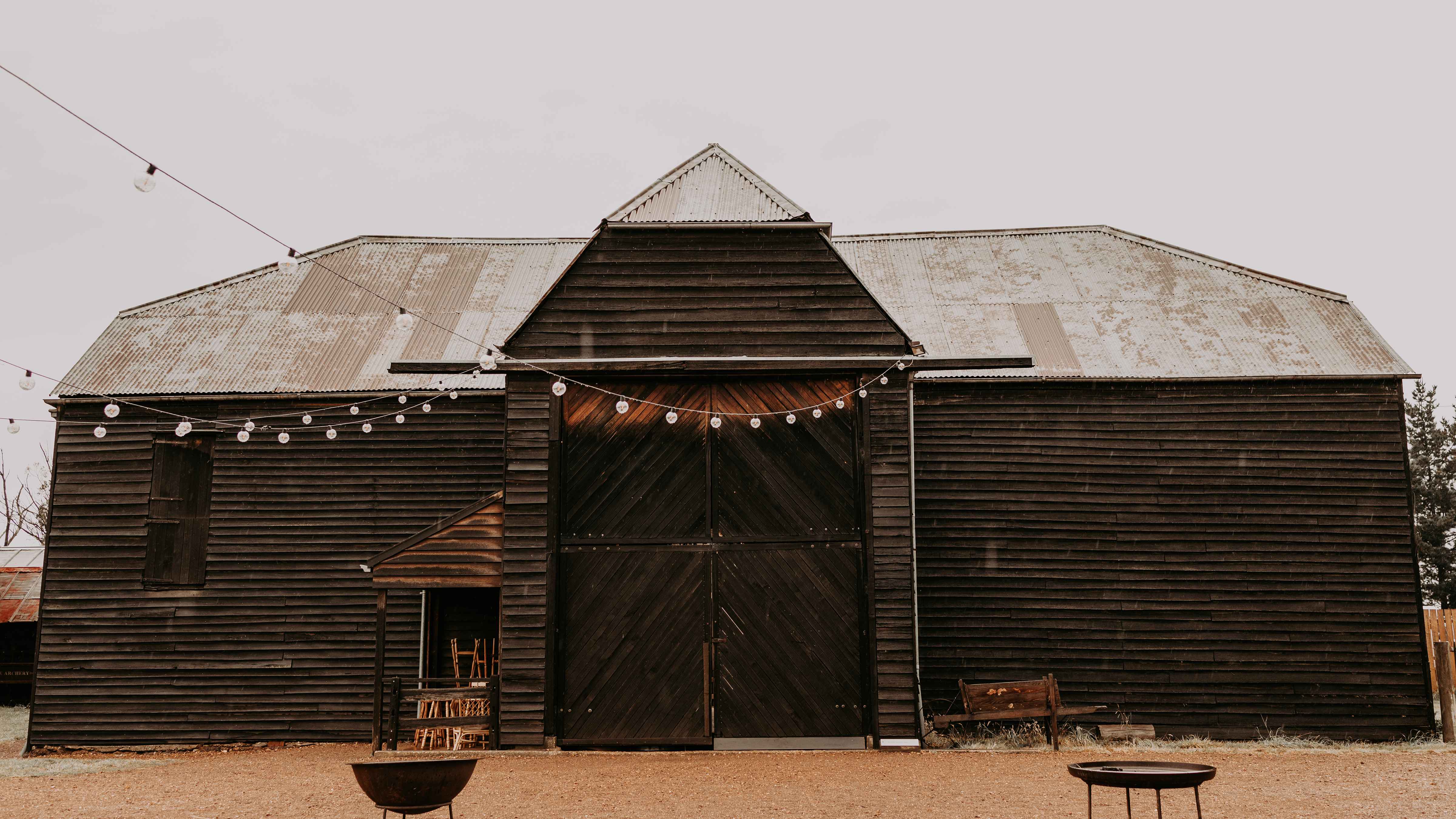 The Sussex Barn made from weatherboards with corrugated iron roof. Festoon lights hang from the barn and two fire pits stand in the quadrangle. Photo: Tiarne Shaw Photography.