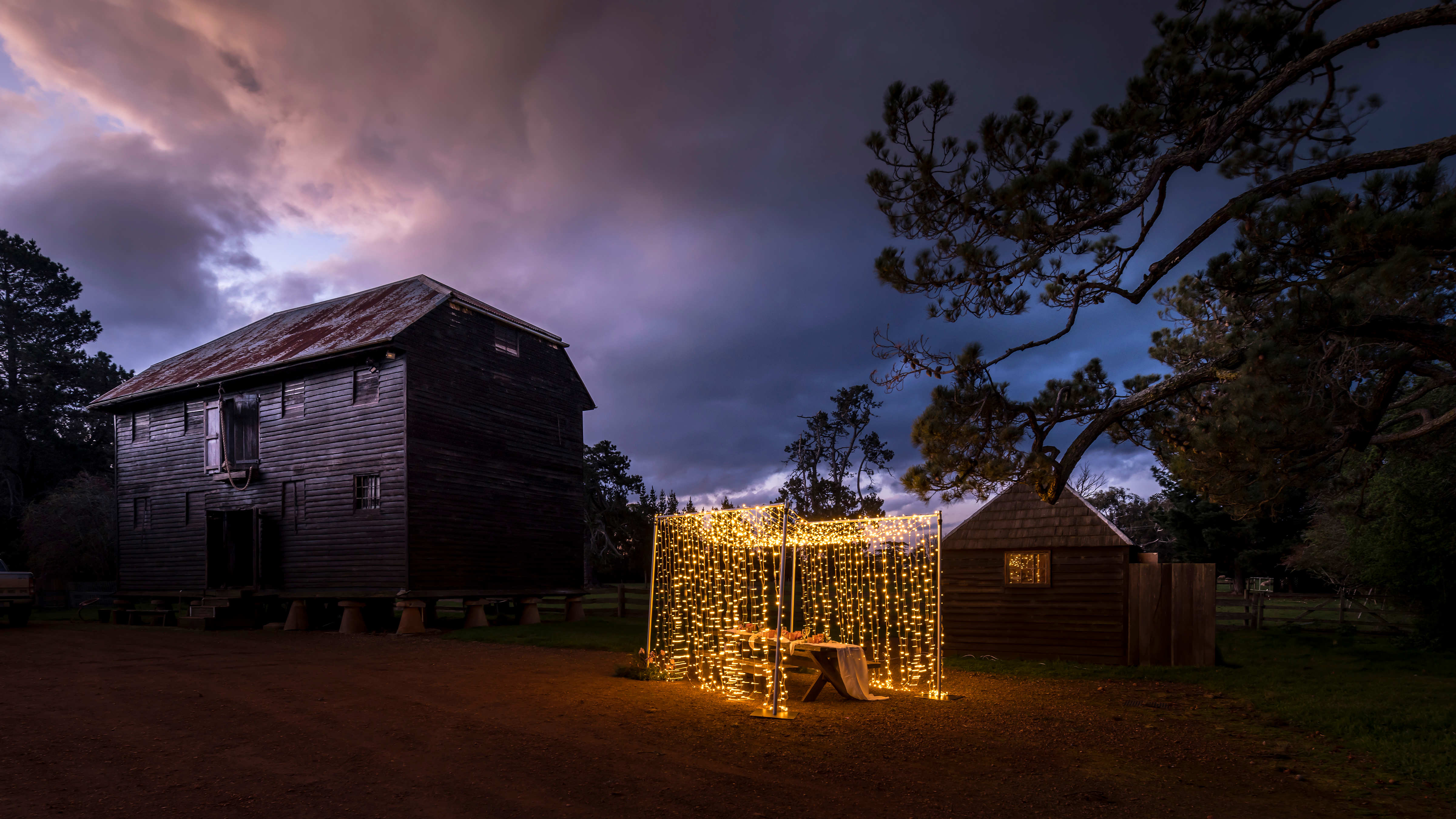The Pillar granary and another small building stand in the shadow as a frame draped with fairy lights sits in front. A pine tree stands to the right of the picture. Photo: Rob Burnett.