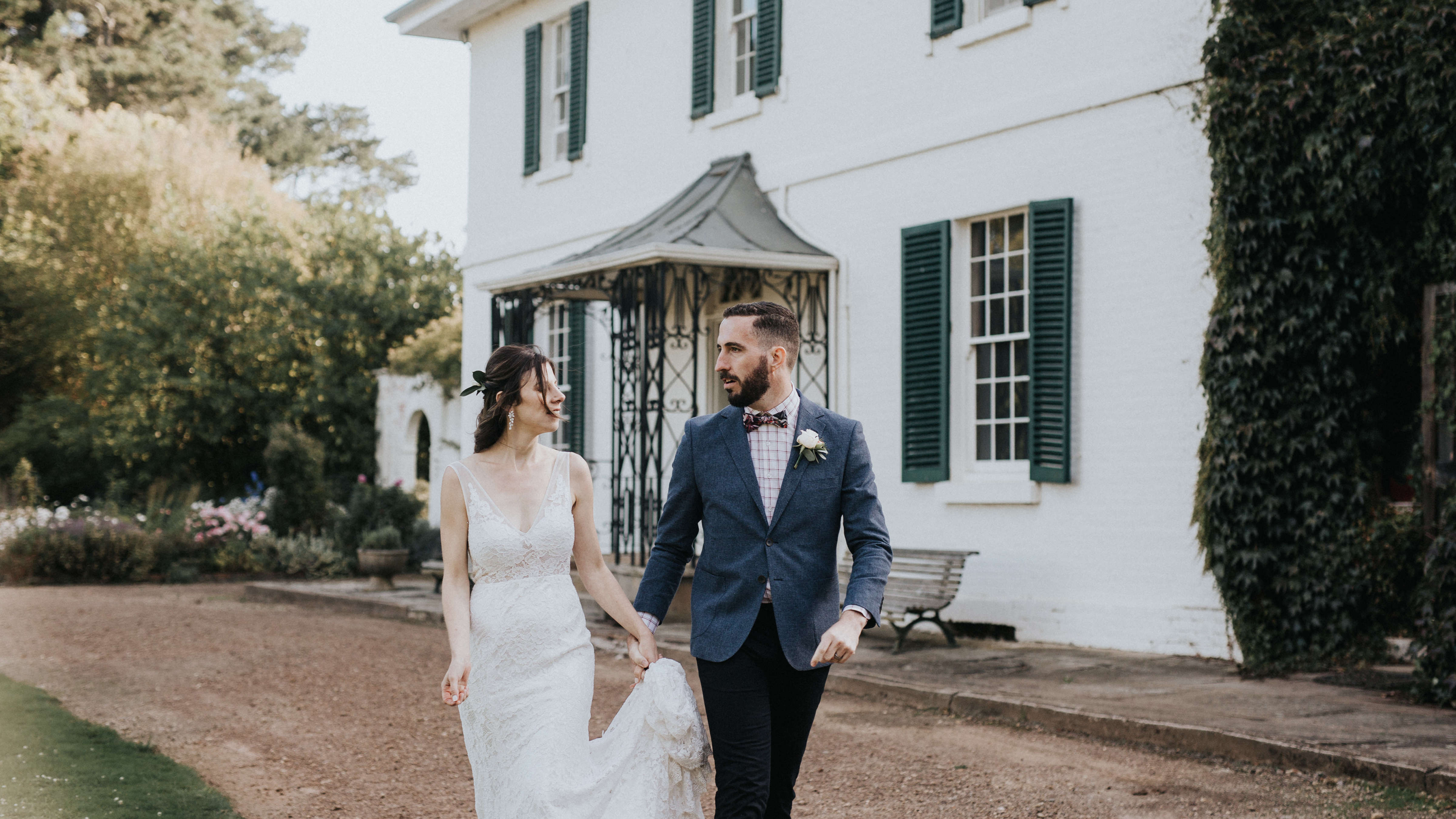 A bride and groom walk along the carriage way in front of the Brickendon Homestead. Boston Ivy covers part of the walls of the house and green shutters frame the Georgian paned windows. Photo: Cassie Sullivan.