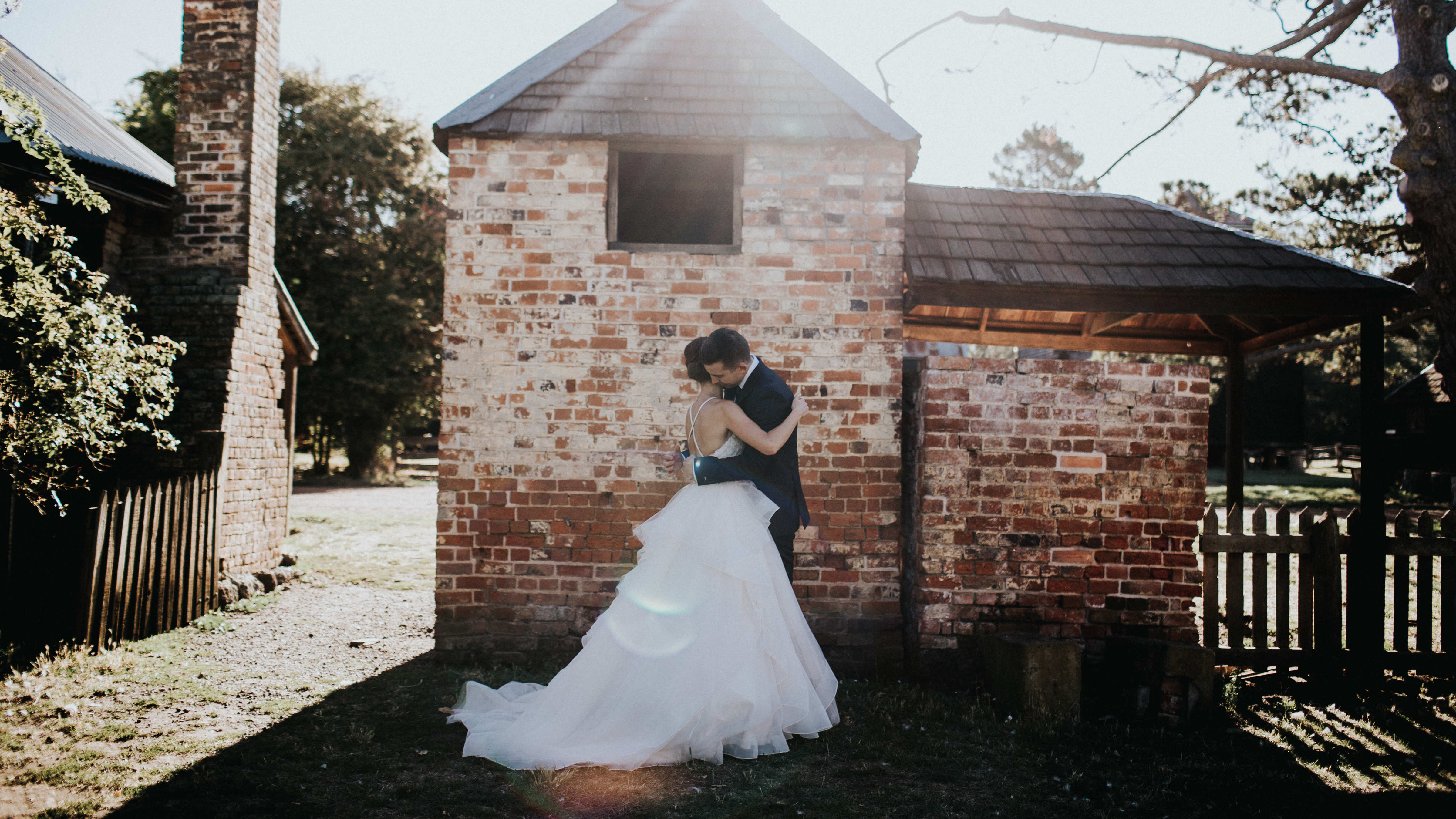 A bride and groom hug in front of the colourful bricks of the smoke house. The William Archer cottage and its brick chimney is to the left of the photo. Photo: Cassie Sullivan.