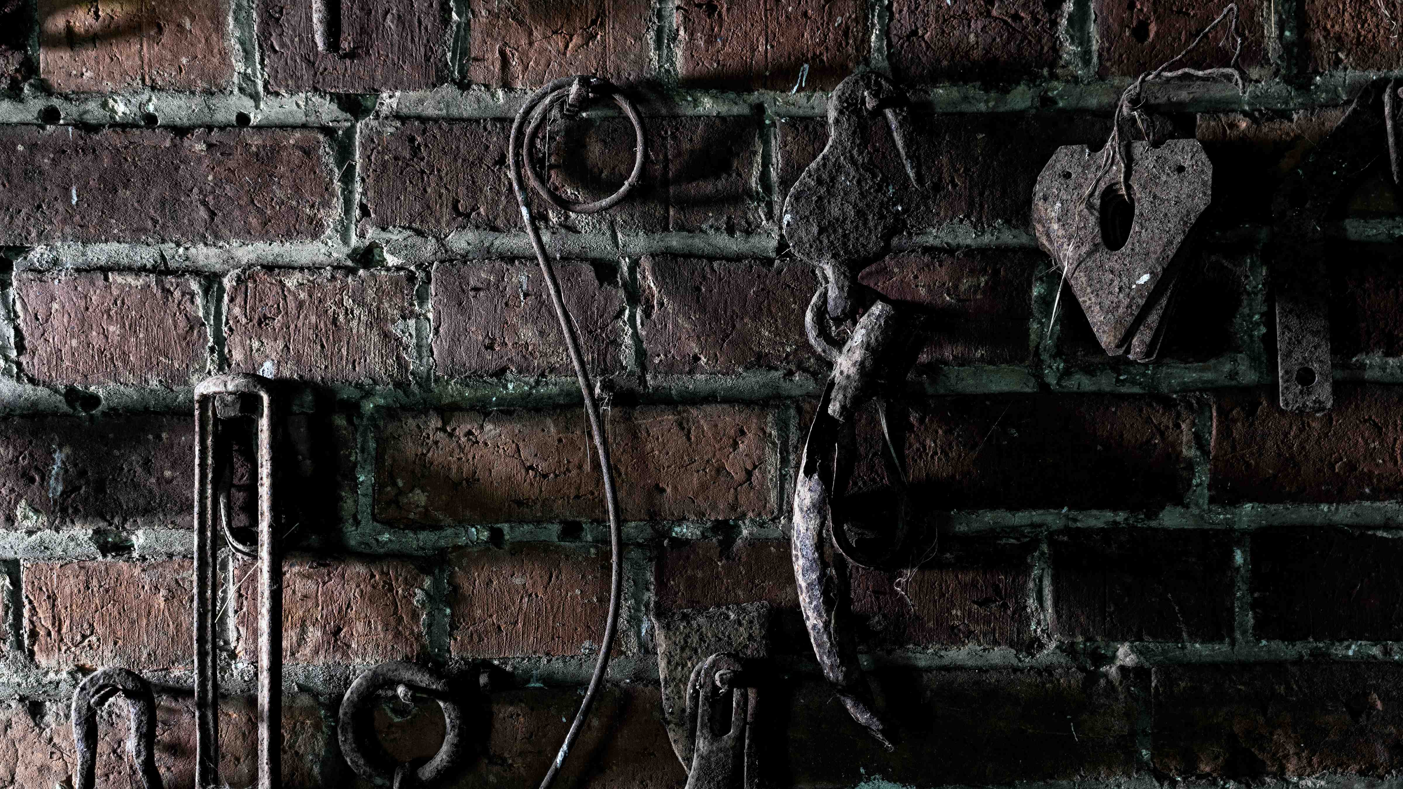 Metal artefacts hang on hooks against an old brick wall. Photo: Rob Burnett.